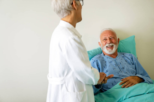 Doctor talking to senior male patient in hospital bed who is recovering from the disease. Healthcare, coronavirus, people concept. - Foto, imagen