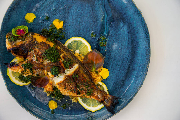 Fried fish with lemon, sauce and green petals in a plate that stands on the table - Photo, Image