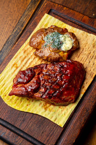 Grilled steak with sauce, potatoes, butter, parsley and pita bread on a wooden board standing on the table - Photo, Image