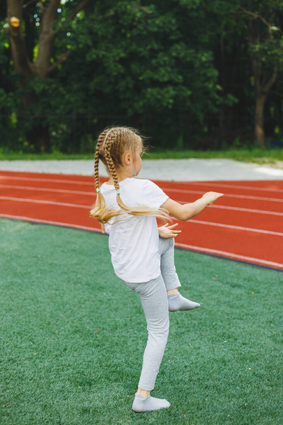 Маленька дівчинка займається спортом на траві, дитина робить розминку перед тренуванням на стадіоні. Дитячий спорт і здоровий спосіб життя
. - Фото, зображення