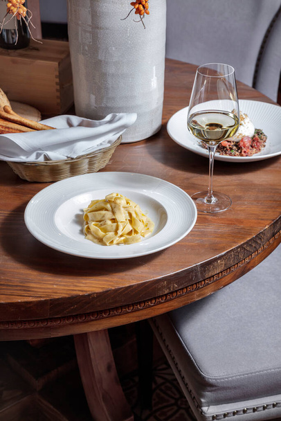 Σπαγγέτι με σάλτσα σε πιάτο σε ξύλινο τραπέζι με ένα ποτήρι κρασί, γκρίζι σε καλάθι και άλλο πιάτο στο φόντο - Φωτογραφία, εικόνα