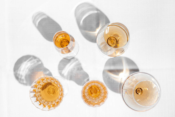 Glasses with rose wine. On a table with a light tablecloth are five glasses of different shapes and sizes with rose wine. A wine cellar is visible in the background. - Foto, afbeelding