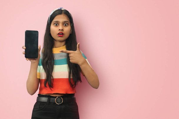 Isolated portrait of Amazed Indian Asian girl pointing finger on Mobile with copy space. - Photo, Image
