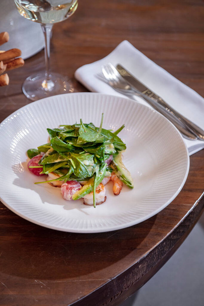 Shrimp salad with sauce, basil and radish in a plate on a wooden table with cutlery and a glass of wine - Foto, Imagen