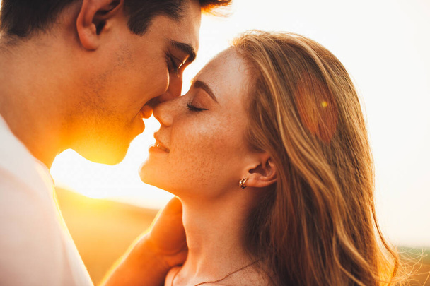 Close-up portrait of a caucasian couple kissing during their date against sunset light, outside. Romantic relationship concept. Love, romance concept. Nature - Zdjęcie, obraz