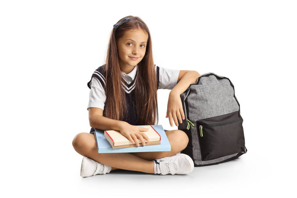 Iskoláslány ül a padlón egy könyvet az ölében, és támaszkodik a hátizsák elszigetelt fehér háttér - Fotó, kép