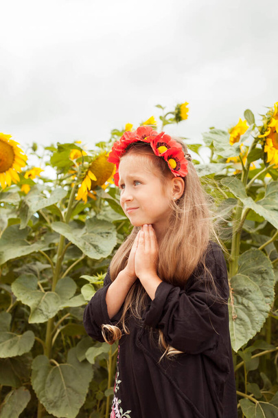 A beautiful Ukrainian girl. Ukrainian girl in the field. A child in an embroidered dress. Ukrainian woman Run across Ukrainian land. Girl's flower wreath. - Photo, image