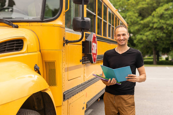 handsome teacher looking at camera school bus blurred on background. - Фото, изображение