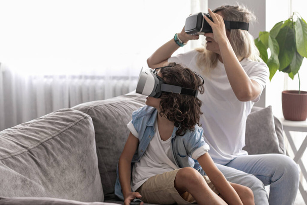 Anne ve oğlu sanal gerçeklik kulaklığı takıyor evdeki oturma odasında sanal gerçeklik oyunları oynayarak eğleniyorlar. - Fotoğraf, Görsel