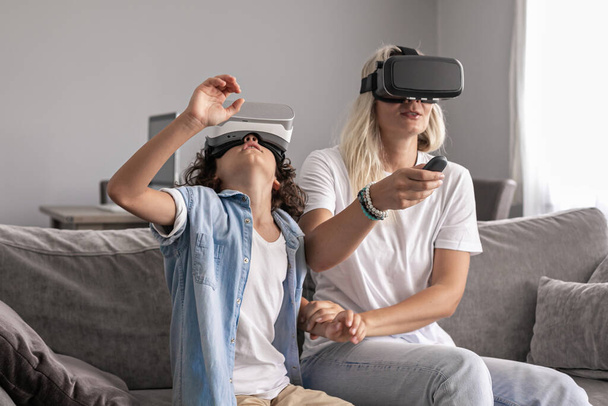 Anya és fia visel virtuális valóság headset vr szemüveg a nappaliban otthon szórakozás kölcsönhatásban virtuális valóság játék játékok - Fotó, kép