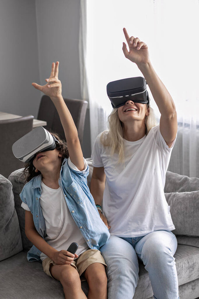 Mother and son wearing virtual reality headset vr glasses in living room at home having fun interacting with virtual reality playing games - Photo, Image