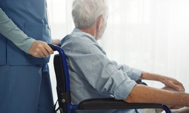 Nurse putting wheelchair with senior man  window. Unhappy senior man having geriatric or depression disease. Therapist taking care, giving support and empathy. - Photo, Image