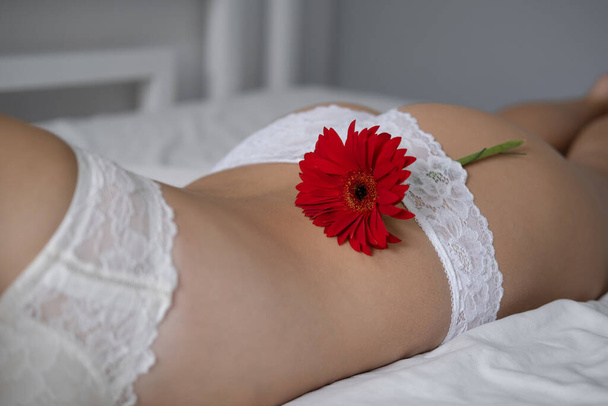 Widok na młodą kobietę w koronkowych majtkach z kwiatem w pobliżu bielizny na łóżku. Epilować strefę bikini. oncept zdrowia kobiet, reprodukcji, ginekologii. spa ciało piękno nogi.  - Zdjęcie, obraz