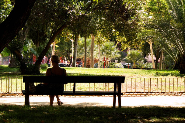 Young woman resting on a bench in a city garden on a sunny day - Φωτογραφία, εικόνα