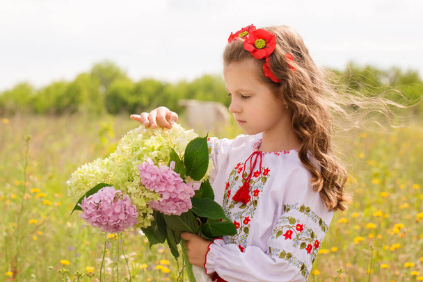 Tyttö ukrainalaisessa kansanpuvussa pellolla hortensiakimpun kanssa. - Valokuva, kuva