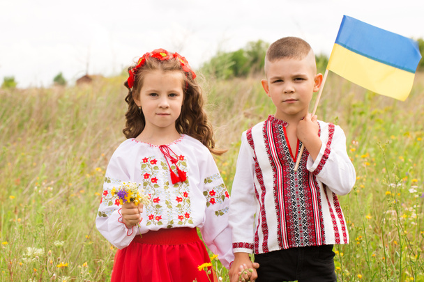 Kisfiú és lány nemzeti ukrán ruhában, kék-sárga zászlóval a mezőn. A szabad Ukrajna koncepciója - Fotó, kép