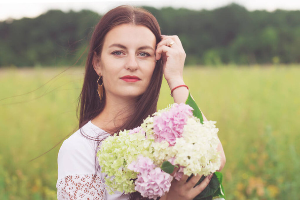 Kaunis nuori nainen kukkakimppu hortensiat alalla - Valokuva, kuva