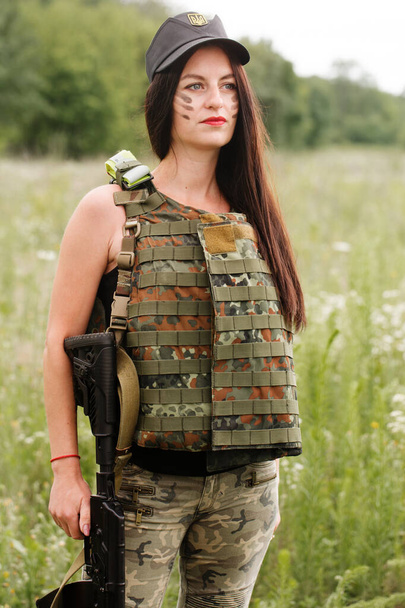 Ukrainian female military servicewoman with a machine gun in her hands in the middle of a field - Фото, изображение