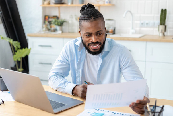 Portrait of confident African American businessman freelancer analyzing annual sales chart. Man working remotely from home - Fotografie, Obrázek