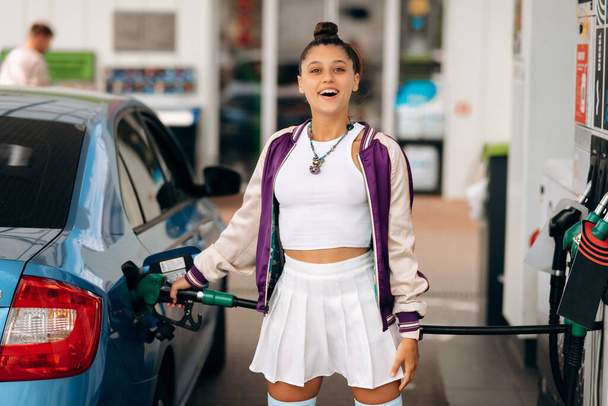 Cheerful young woman brunette filling her car with fuel at a gas station - 写真・画像
