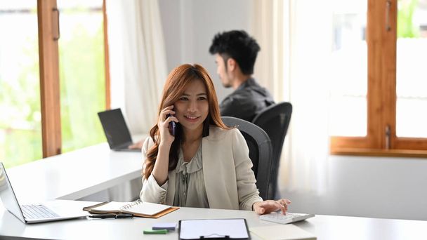 Atrakcyjna kobieta doradca finansowy prowadzący negocjacje z klientem przez telefon komórkowy. - Zdjęcie, obraz