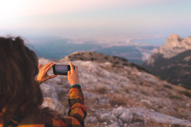 beautiful young girl travels and takes a photo on the phone. travel in the mountains. portrait of a girl with a phone at sunset. - Foto, Imagem