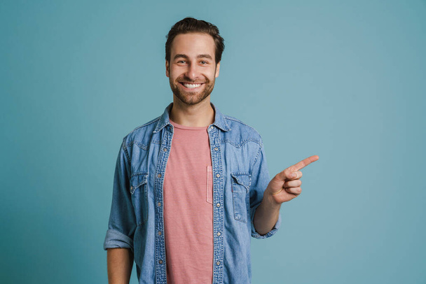 Young bristle man wearing shirt smiling and pointing finger aside isolated over blue background - Φωτογραφία, εικόνα