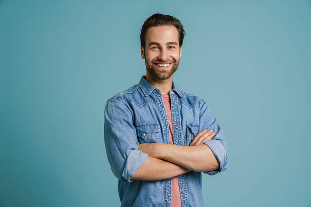Young bristle man wearing shirt smiling while posing with arms crossed isolated over blue background - Fotoğraf, Görsel