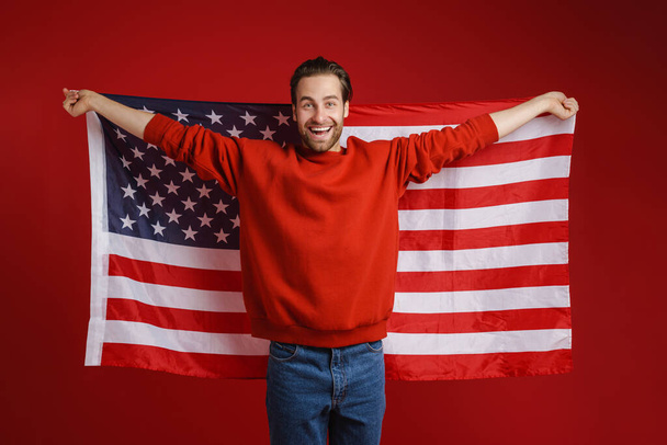 Young bristle man smiling while posing american flag isolated over red background - Fotografie, Obrázek