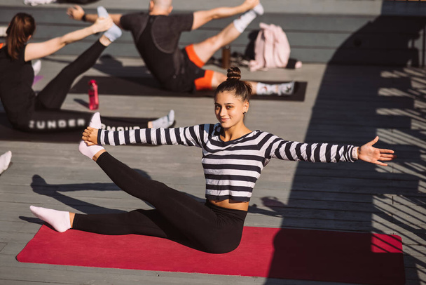 Yogi vrouw en diverse groep van jonge sportieve mensen beoefenen yoga, vrouwelijke studenten trainen in huizen dak. Welzijn, wellness concept - Foto, afbeelding