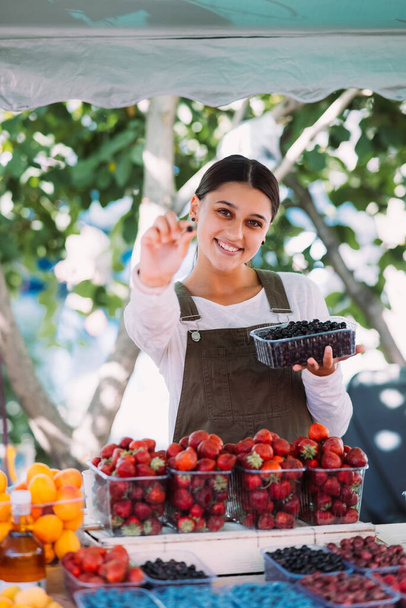 Nuori positiivinen myyjä työpaikalla, myy kotimaisia vihanneksia ja hedelmiä vihanneskaupassa - Valokuva, kuva