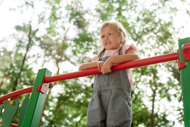 Маленька дівчинка стоїть на дитячому майданчику в літній день
  - Фото, зображення