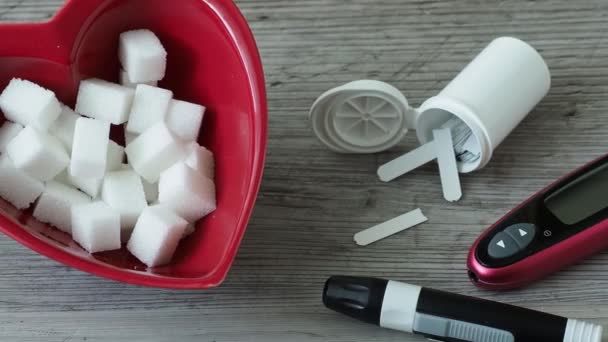 Sugar cubes in a heart shaped bowl. Diabetes testing kit - Imágenes, Vídeo