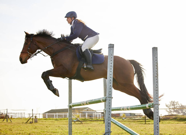 Neem de teugels en vlieg. een jonge ruiter springt over een horde op haar paard - Foto, afbeelding