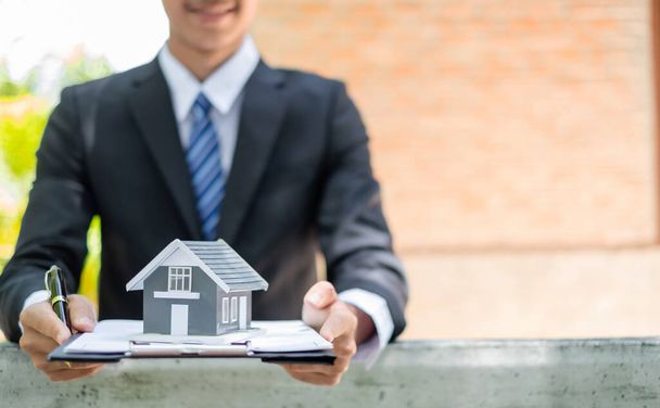 Home insurance concept and real estate. Business Asian man holding a house model working in investment about renting a house, buying a house, and home insurance. - Φωτογραφία, εικόνα