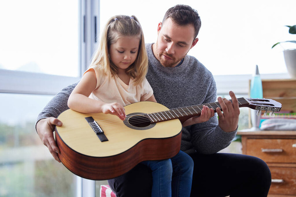 Teaching her some chords. a young father teaching his daughter to play the guitar at home - 写真・画像