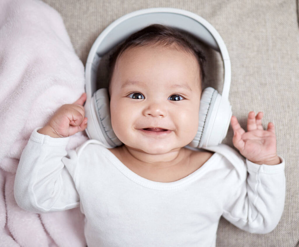 Music is great for a babys learning and development. High angle shot of an adorable baby wearing headphones at home - Valokuva, kuva