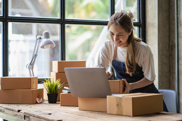 Small business start-up, SME, owner of an Asian female entrepreneur uses a laptop to receive and check online orders to prepare packing boxes. Selling ideas online, shipping parcels. - Foto, immagini
