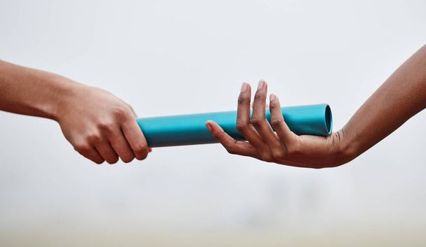 Passing the baton to future generations. two athletes passing a baton during a relay race - 写真・画像