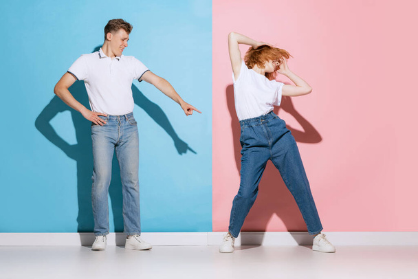 Pembe mavi stüdyo arka planında izole bir şekilde dans eden genç çiftin portresi. Sıradan giysili mankenler. Gençlik kavramı, duygular, yüz ifadesi, aşk, ilişki. Poster, reklam - Fotoğraf, Görsel