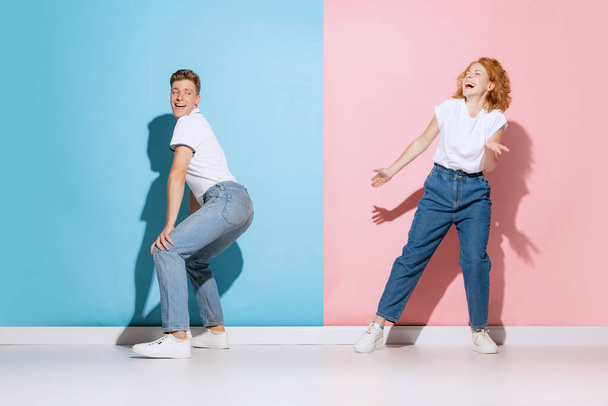 Portrait of young emotive couple, cheerfully dancing, posing isolated over pink blue studio background. Good mood. Concept of youth, emotions, facial expression, love, relationship. Poster, ad - Foto, Imagem