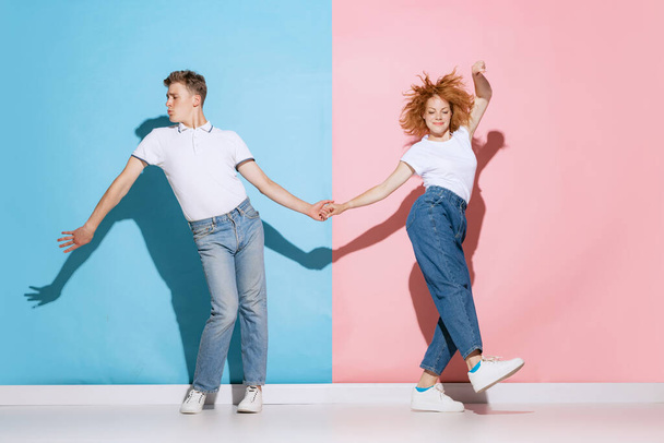 Portrait of young couple holding hands, dancing boogie woogie isolated over pink blue studio background. Concept of youth, emotions, facial expression, love, relationship. Poster, ad - Foto, afbeelding