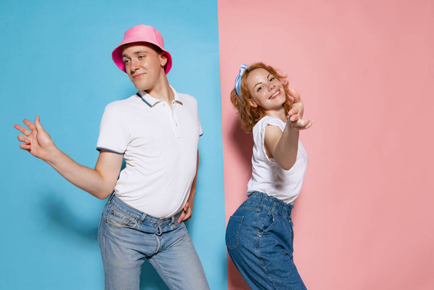 Portrait of young man and woman, couple in casual outfit dancing, posing isolated over pink blue studio background. Concept of youth, emotions, facial expression, love, relationship. Poster, ad - Фото, изображение