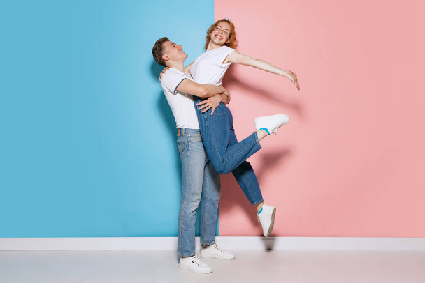 Portrait of young happy and smiling couple, hugging, posing isolated over pink blue studio background. Romantic look. Concept of youth, emotions, facial expression, love, relationship. Poster, ad - Fotó, kép