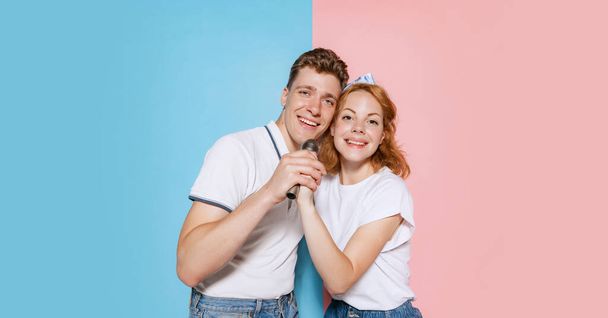 Portrait of young cheerful couple, singing in microphone isolated over pink blue background. Karaoke birthday celebration. Concept of youth, emotions, facial expression, love, relationship. Poster, ad - Φωτογραφία, εικόνα