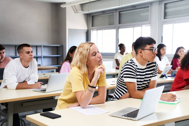 High School Science Class: Ein Junge und ein Mädchen benutzen einen Laptop, während sie den Lehrer in der Klasse betreuen. Eine Gruppe von Schülern lernt im Klassenzimmer. Hochwertiges Foto - Foto, Bild