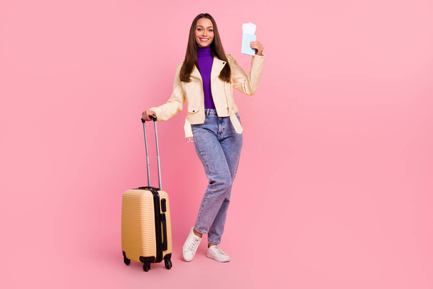 Full length photo of cute young lady with bag hold tickets wear jacket jeans boots isolated on pink color background. - Zdjęcie, obraz