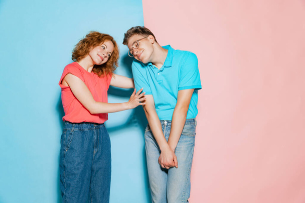 Portrait of young couple, woman saying pleasant words to shy man isolated over pink blue studio background. Cheering up. Concept of youth, emotions, facial expression, love, relationship. Poster, ad - Photo, Image