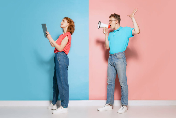 Attention. Portrait of young couple, man shouting in megaphone at working woman isolated over pink blue studio background. Concept of youth, emotions, facial expression, love, relationship. Poster, ad - Zdjęcie, obraz
