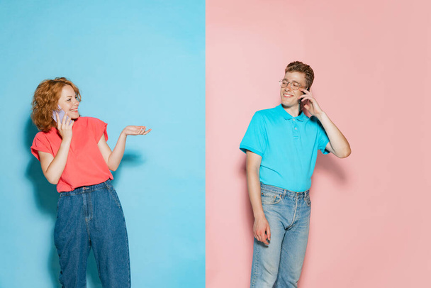 Portrait of young couple, cheerfully talking on phone isolated over pink blue studio background. Excited news spreading. Concept of youth, emotions, facial expression, love, relationship. Poster, ad - Photo, Image